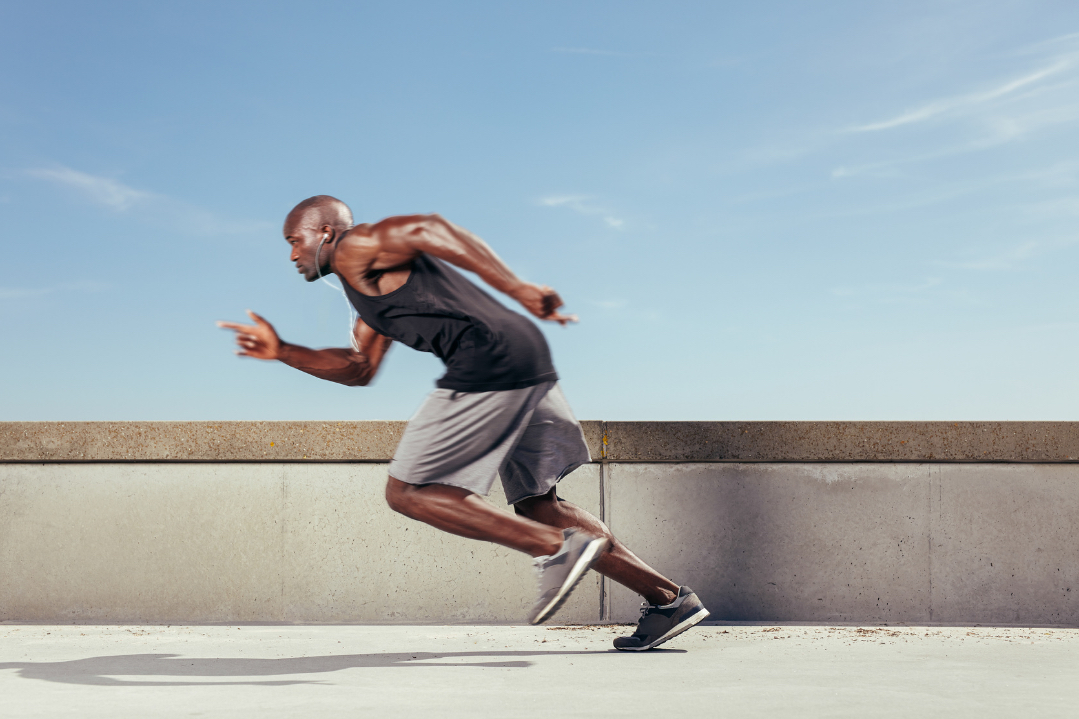 A man sprinting past a concrete wall under a clear blue sky.