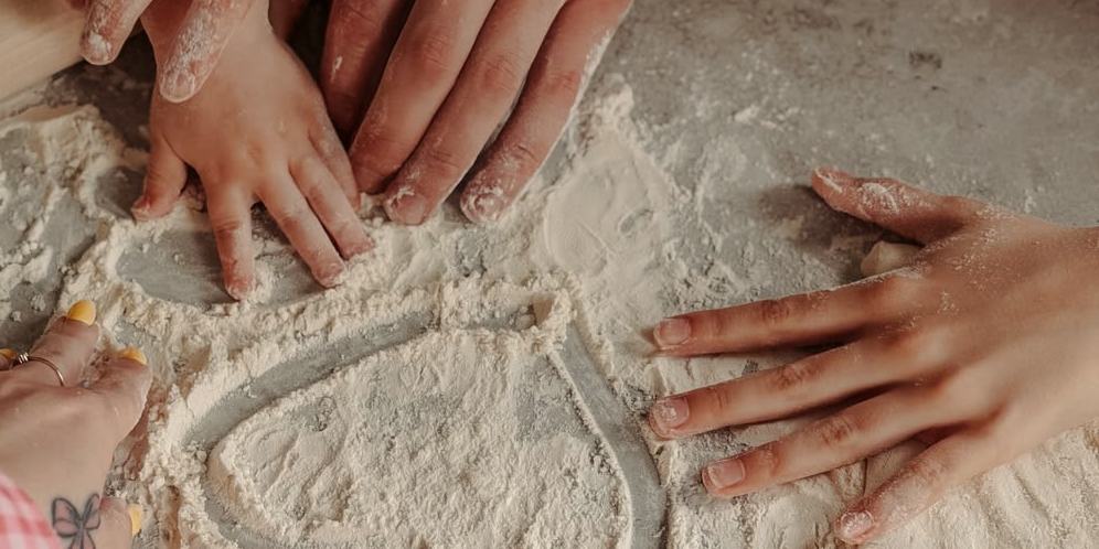 Several pairs of hands working flour on a bench.