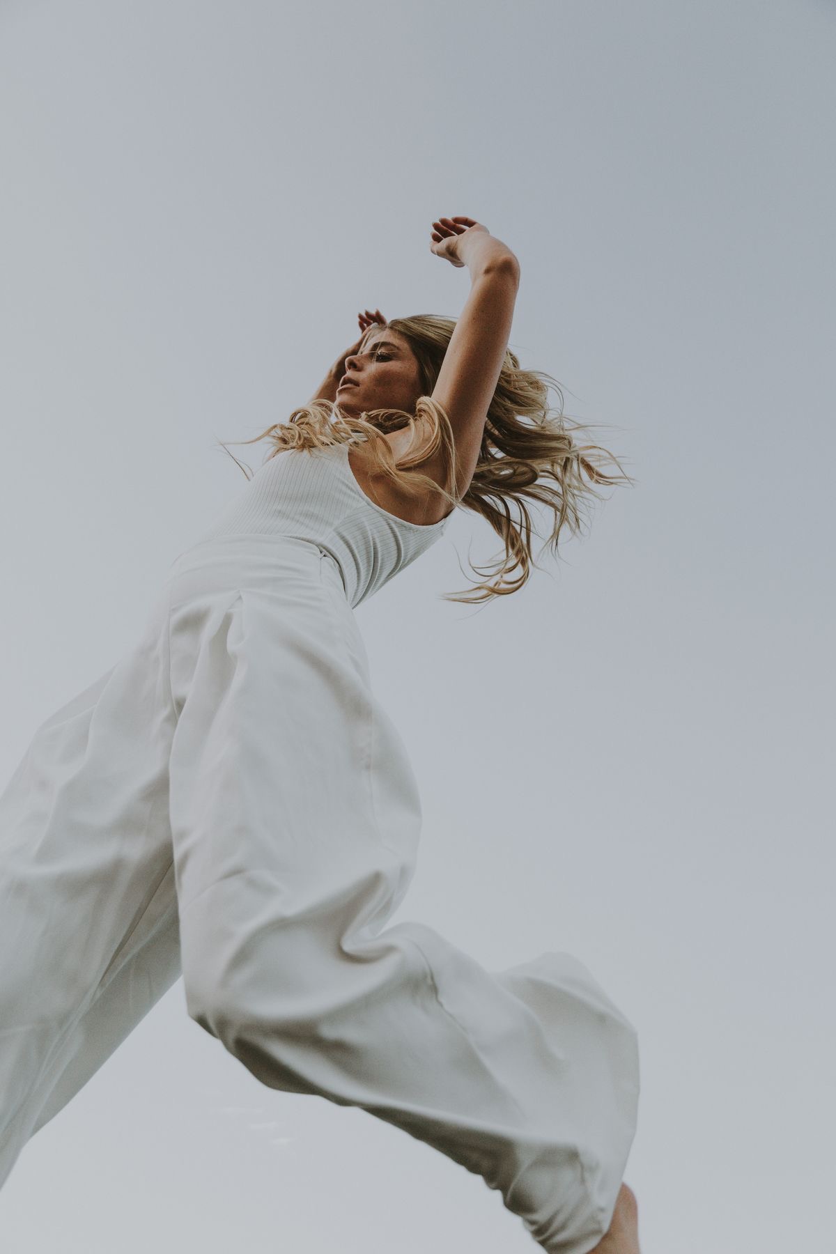 A woman mid jump against an open pale sky, photographed from below.