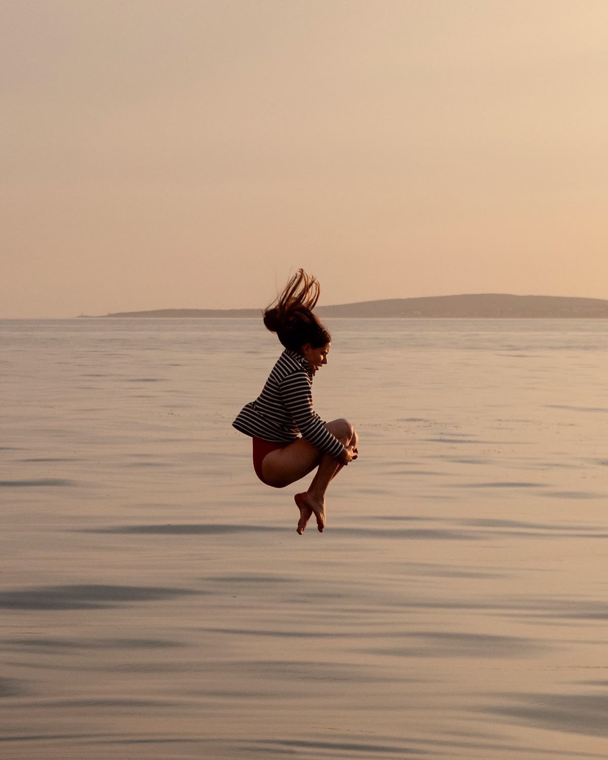 A woman suspended mid jump above still water at dusk.