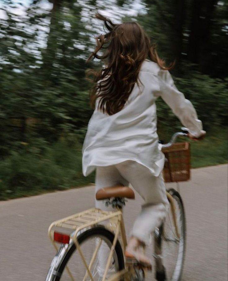A woman riding a bicycle along a tree lined road, caught mid motion.